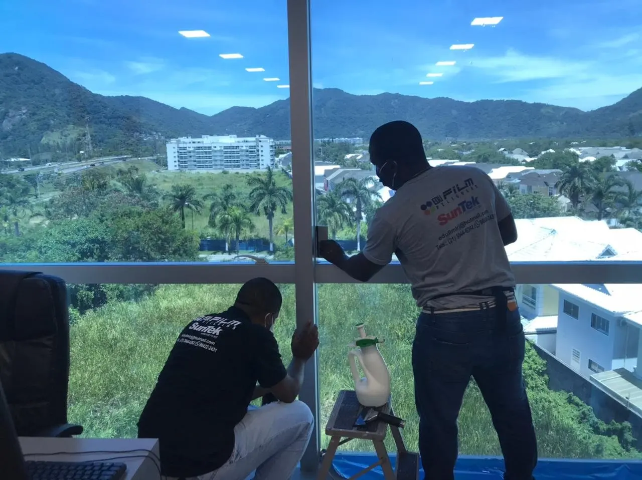 Equipe aplicando película em janela de escritório com vista para a Barra da Tijuca